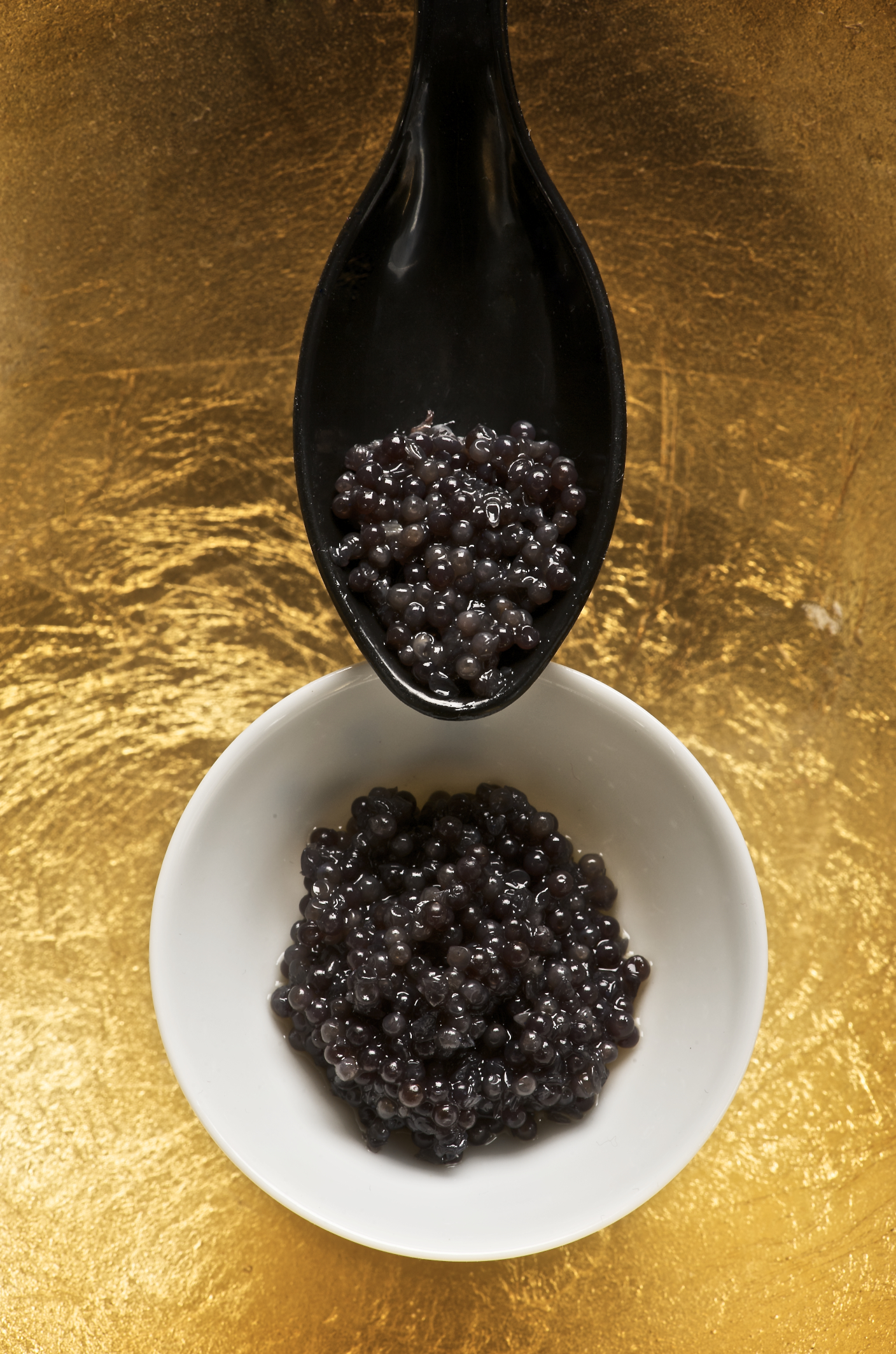 A spoonful of sturgeon caviar is held above a small bowl containing sturgeon caviar.