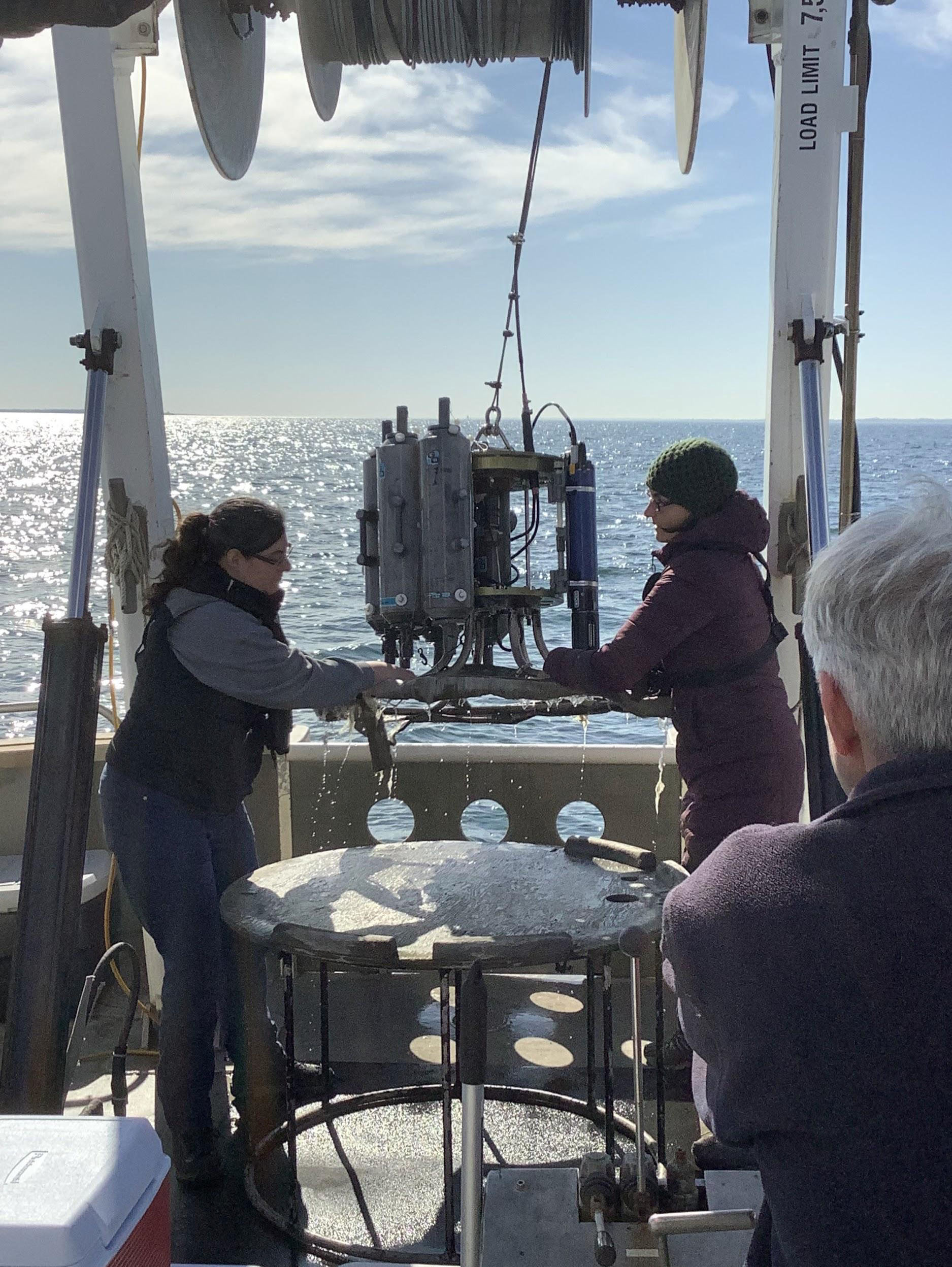 Dr. Vlahos and Katie O'Brien-Clayton retrieve the CTD rosette containing water samples while aboard the research vessel John Dempsey. Water samples are collected using the rosette sampler which holds up to ten niskin bottles, which are set to collect samples at different depths.