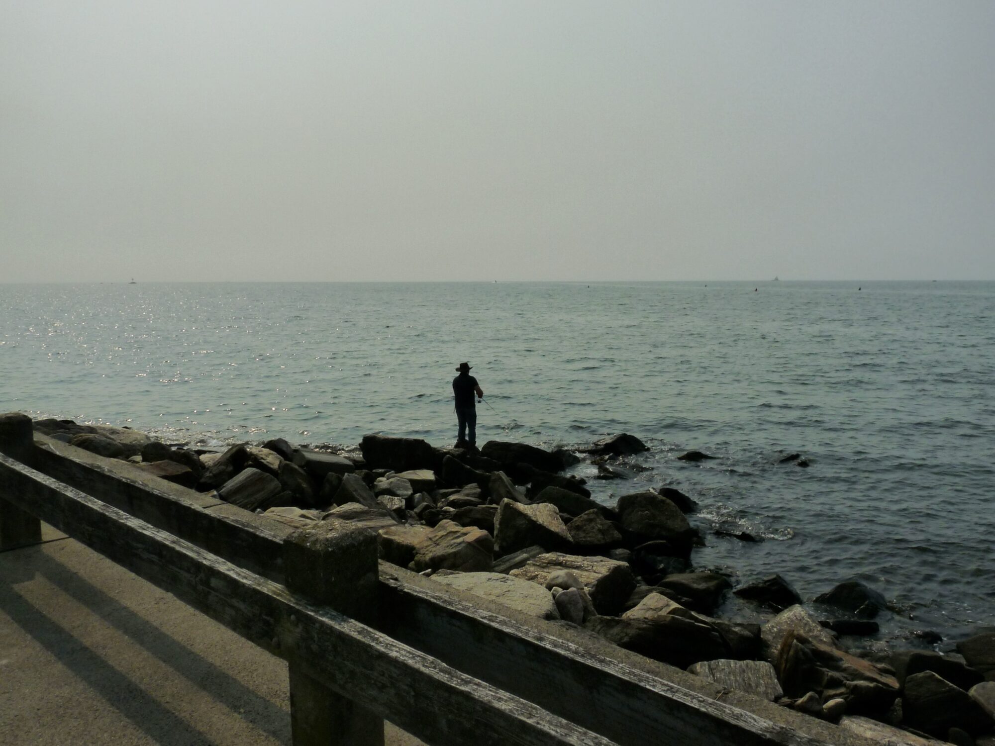 A shadow of a man standing on a  jetty fishing in water. 